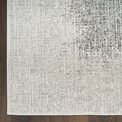Rectangular light gray-beige rug with subtle charcoal speckle and a darker upper-right area on a wood floor.