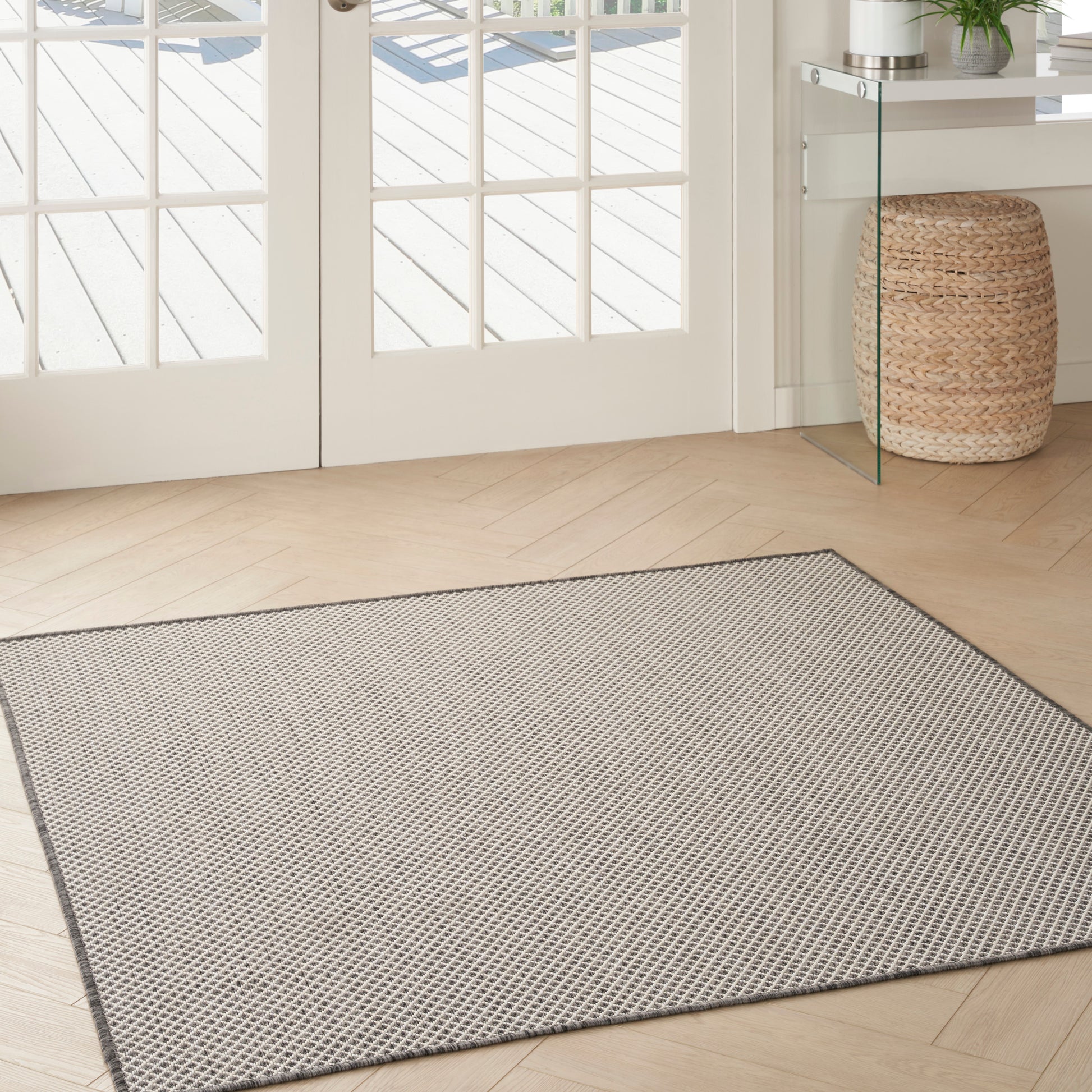 Rectangular light gray textured area rug with a darker border in a bright entryway with French doors & woven basket.