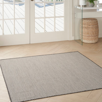 Rectangular light gray textured area rug with a darker border in a bright entryway with French doors & woven basket.