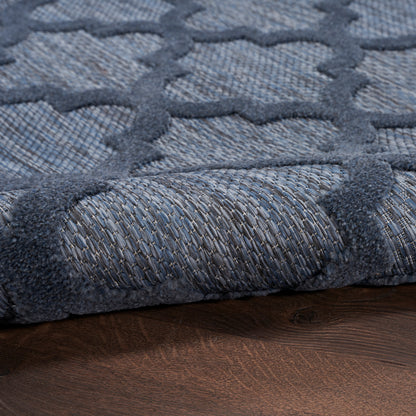 Blue-gray rug with geometric lattice pattern and soft woven pile, rolled edge on wood floor.