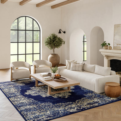 Neutral living room with arched window, cream sofa and chairs, light wood coffee table, and a blue patterned rug.