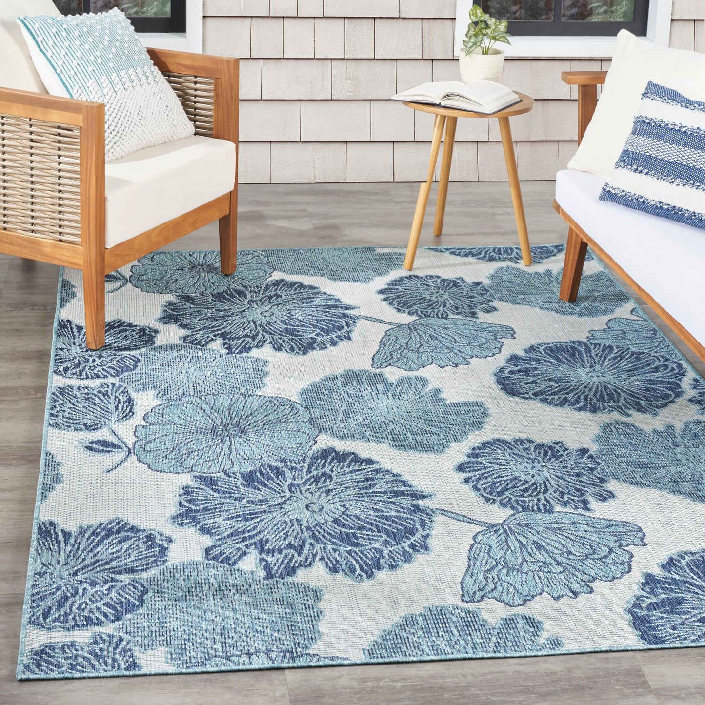 Blue floral area rug with large leaf shapes on light background; wood-framed chairs with white cushions and a round table.