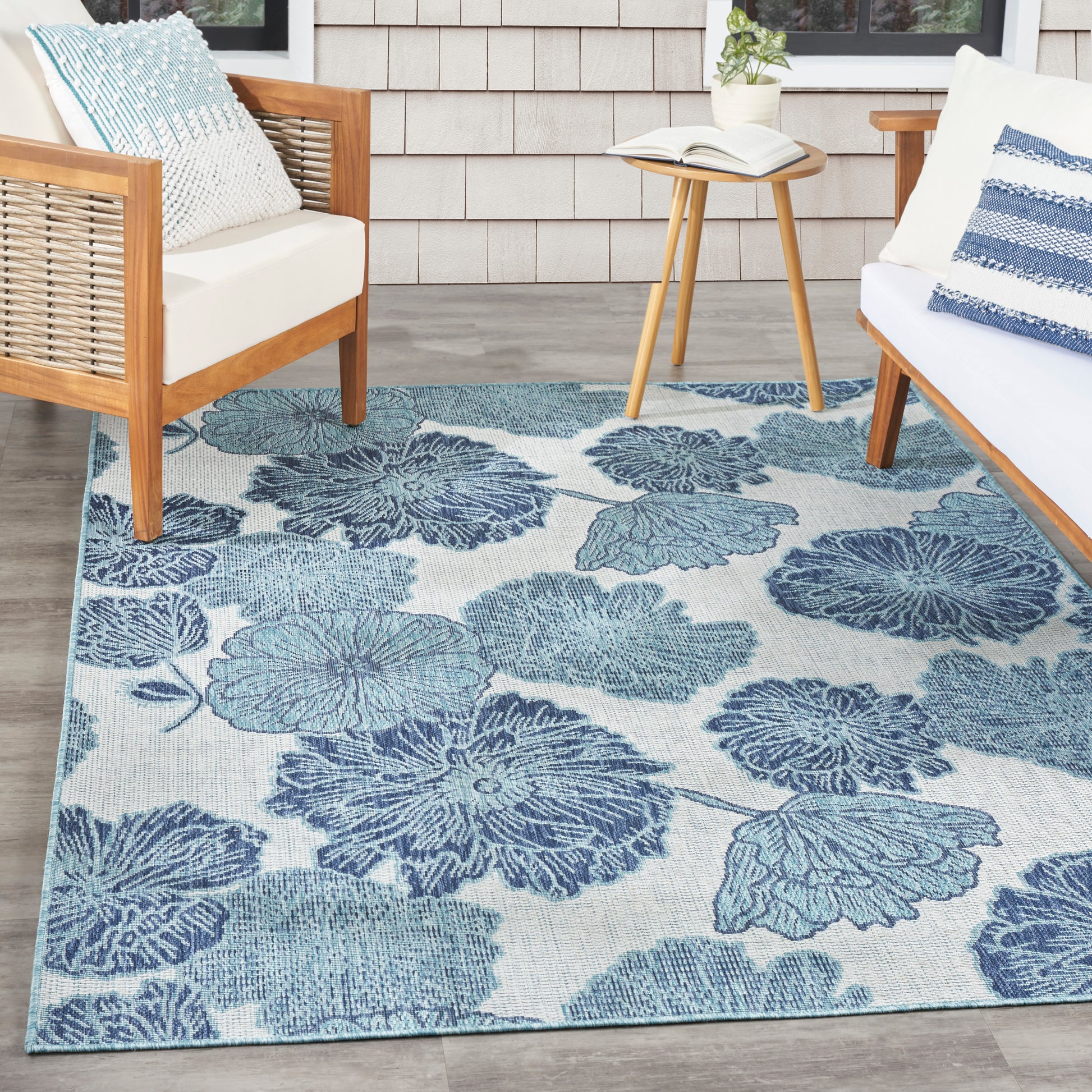 Blue floral area rug with large leaf shapes on light background; wood-framed chairs with white cushions and a round table.