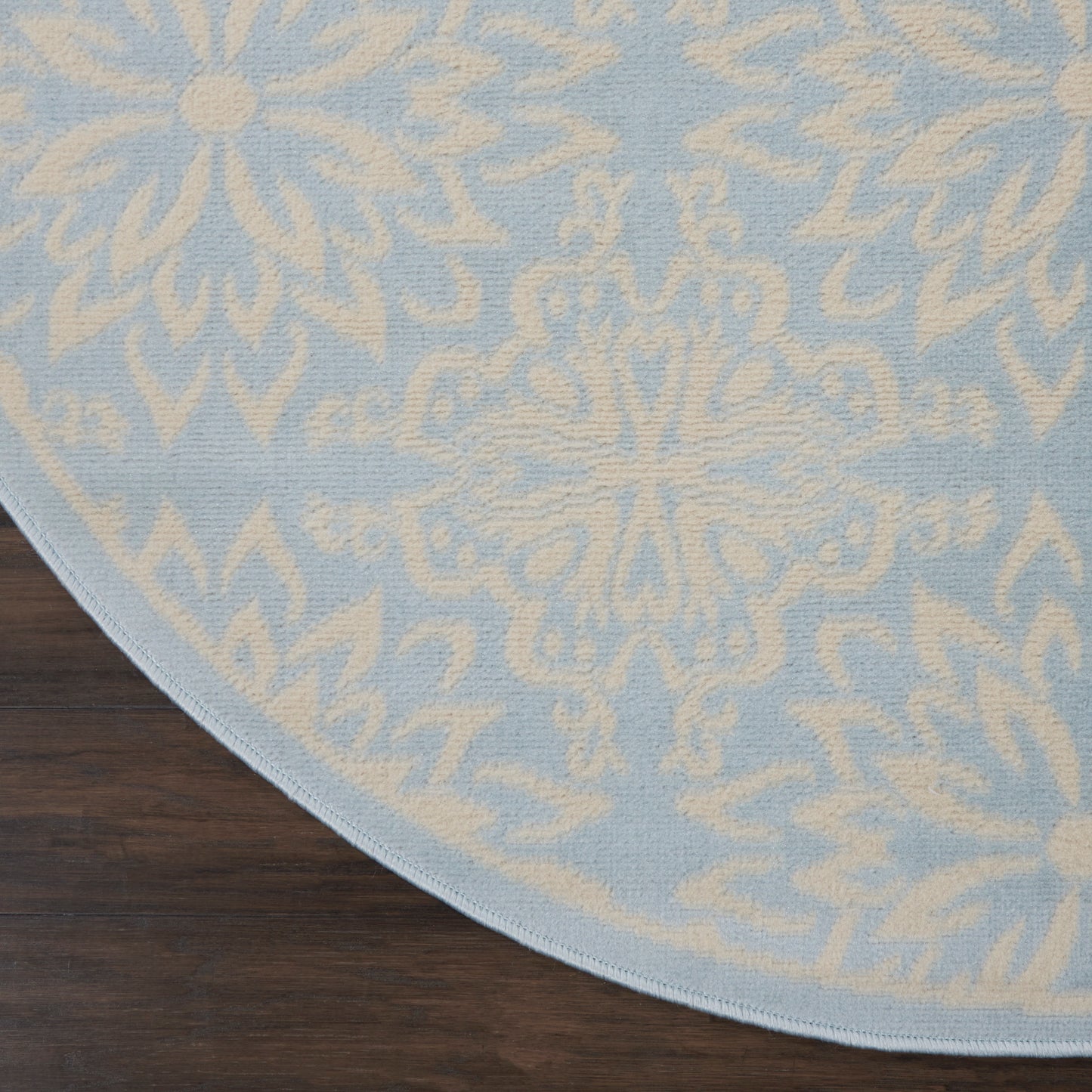 Round blue rug with ivory damask pattern, soft woven texture, light edge binding on dark wood floor.