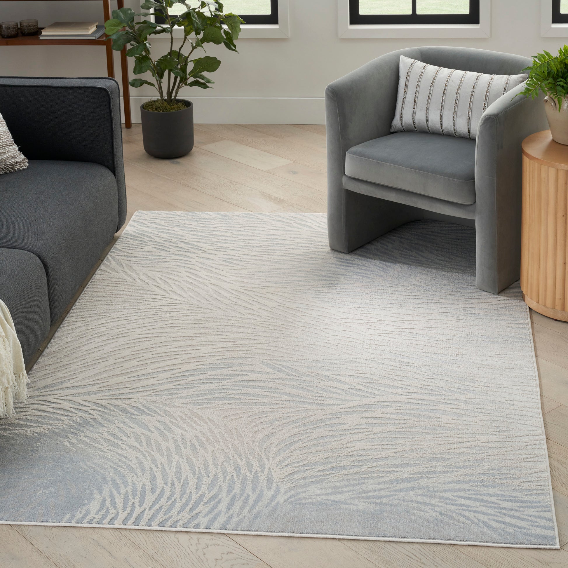 Light gray area rug with pale palm-leaf pattern in a modern living room with gray sofa, armchair and plants.