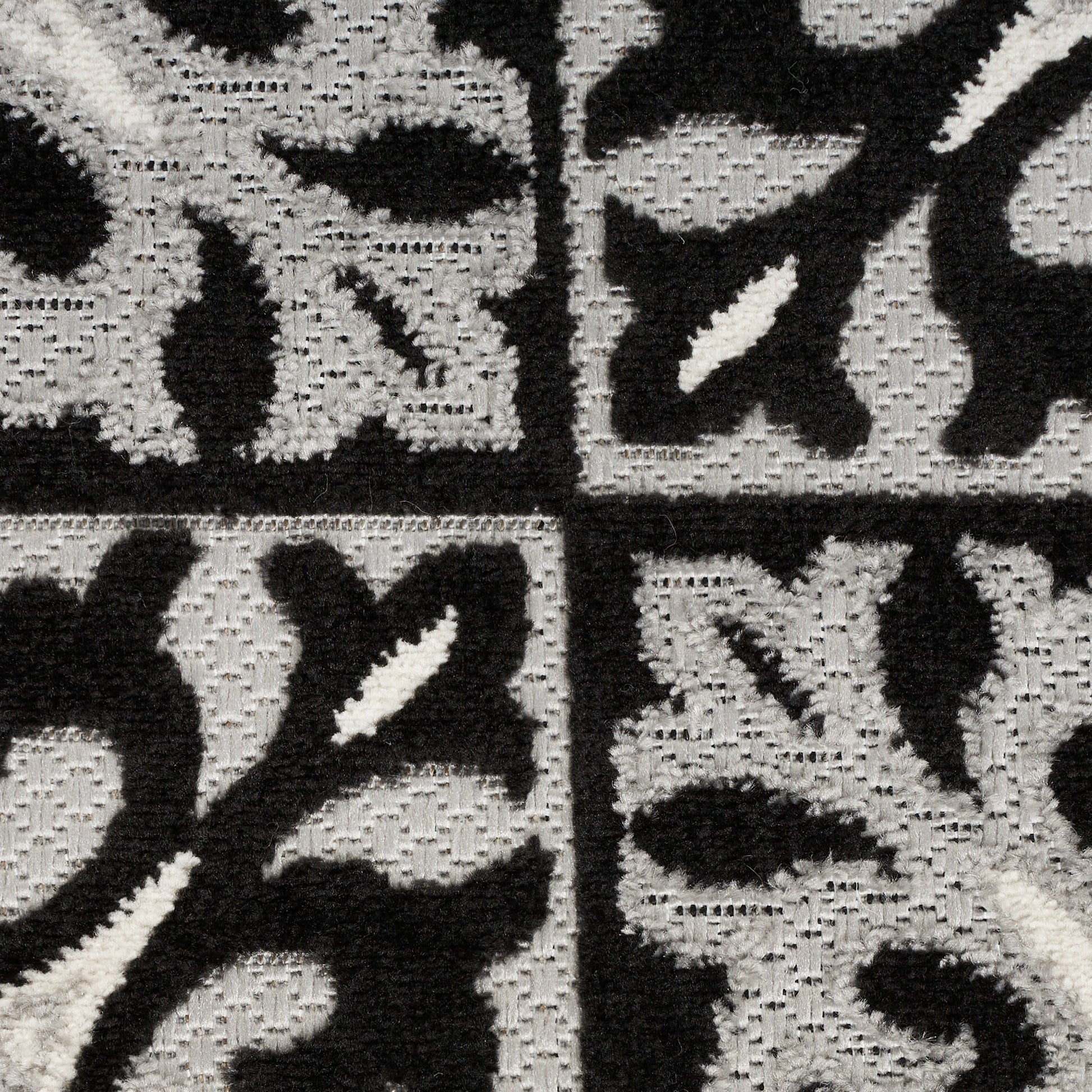 Close-up of a black and gray woven rug with damask floral tile pattern and textured grid.