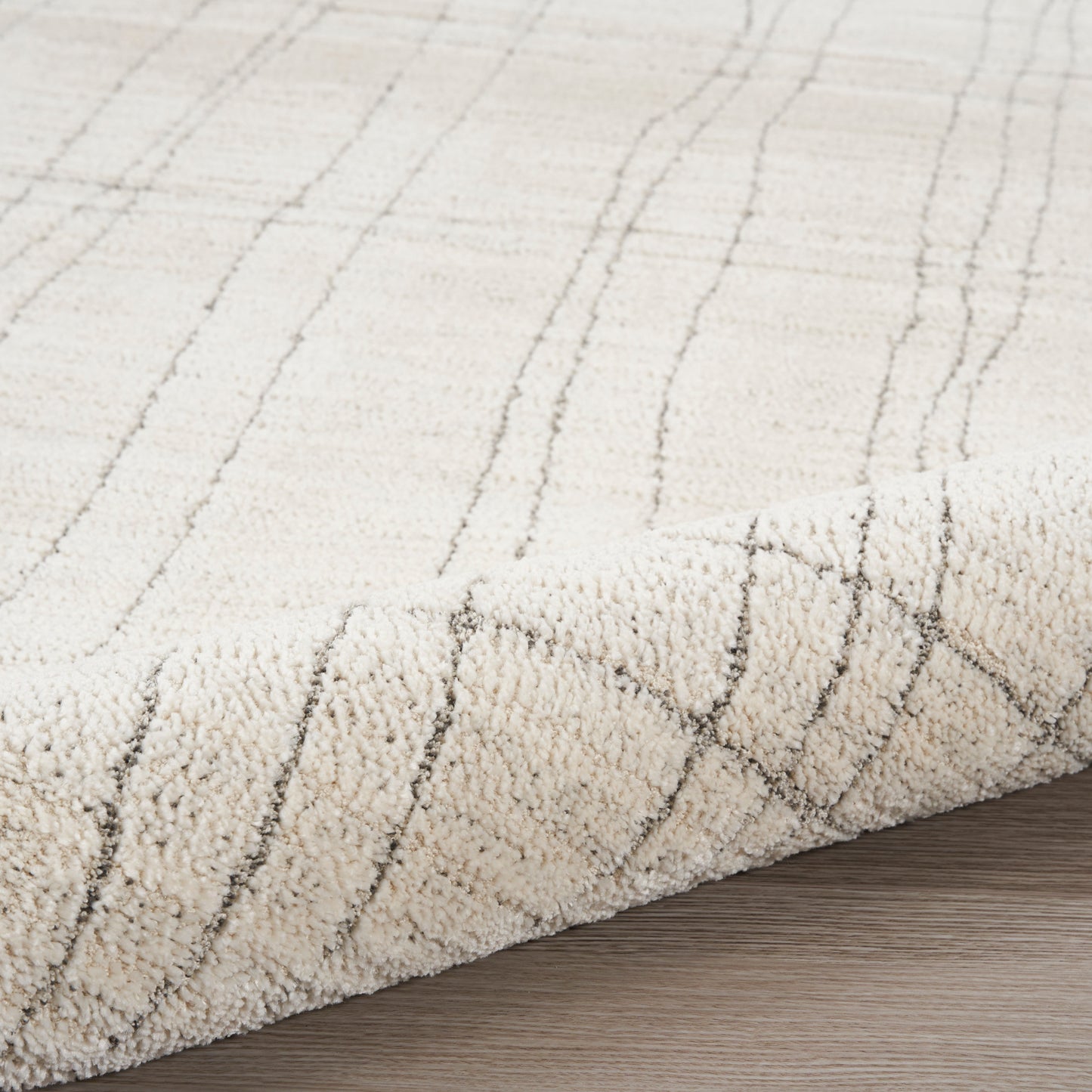 Cream shag rug with subtle gray linear grid pattern, plush pile, folded edge on wood floor.