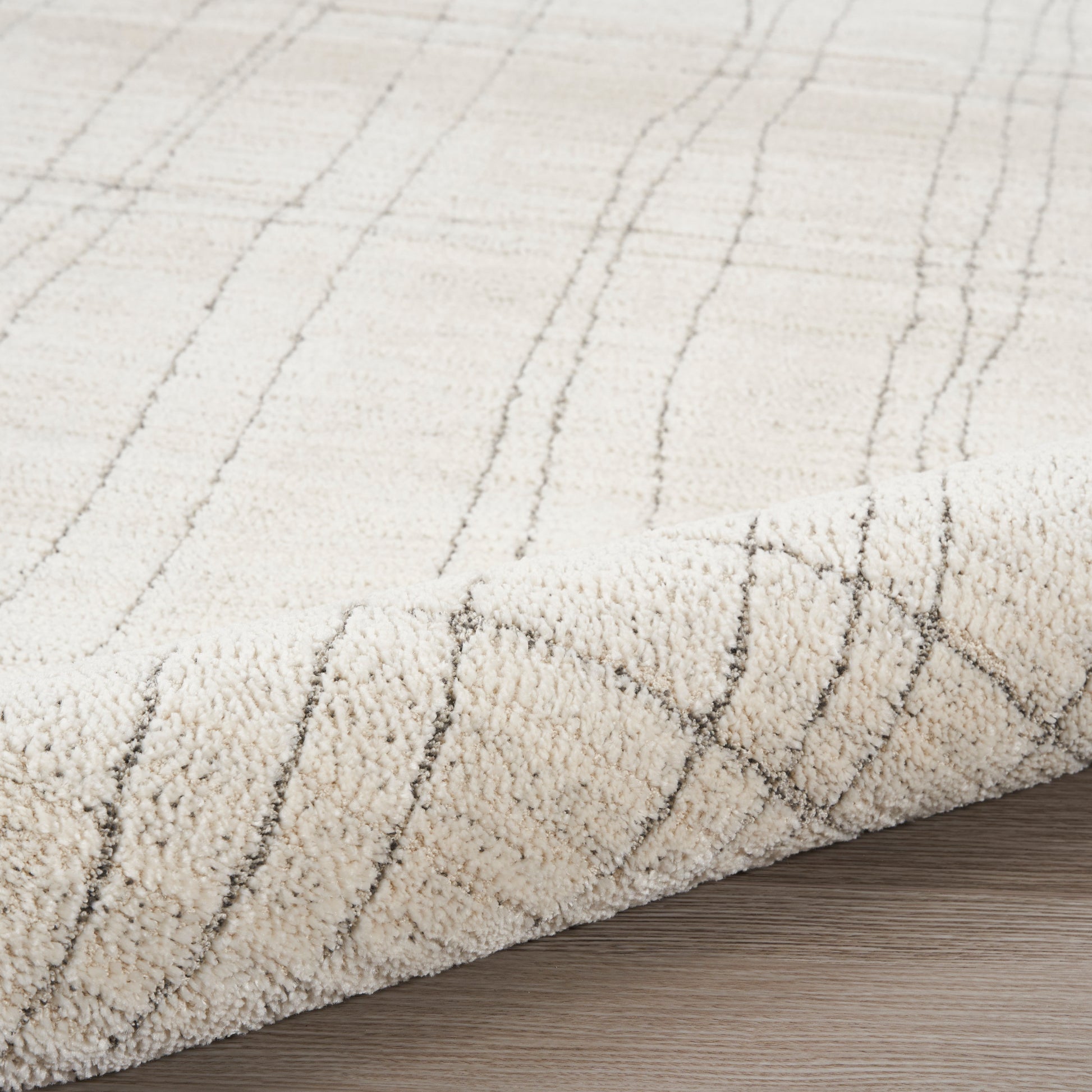 Cream shag rug with subtle gray linear grid pattern, plush pile, folded edge on wood floor.