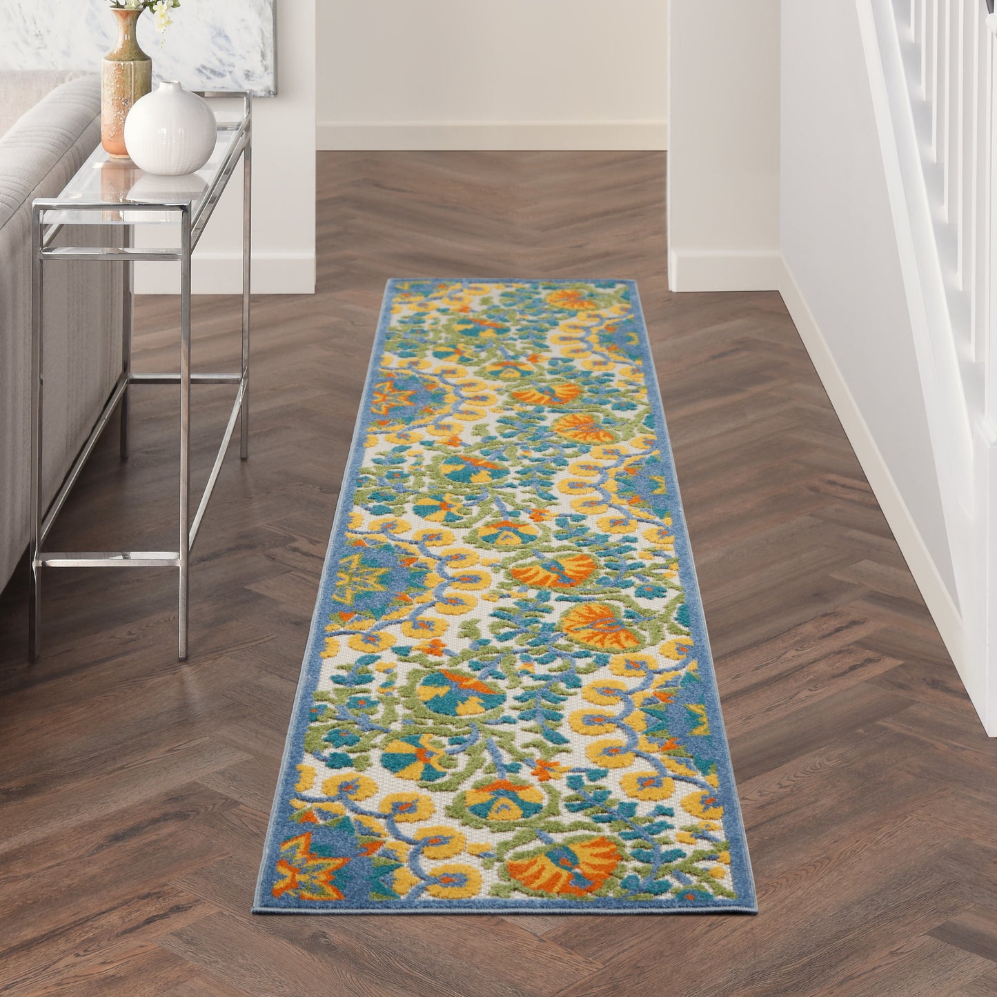 Rectangular floral hallway runner rug in teal, orange, yellow and ivory with a blue border.