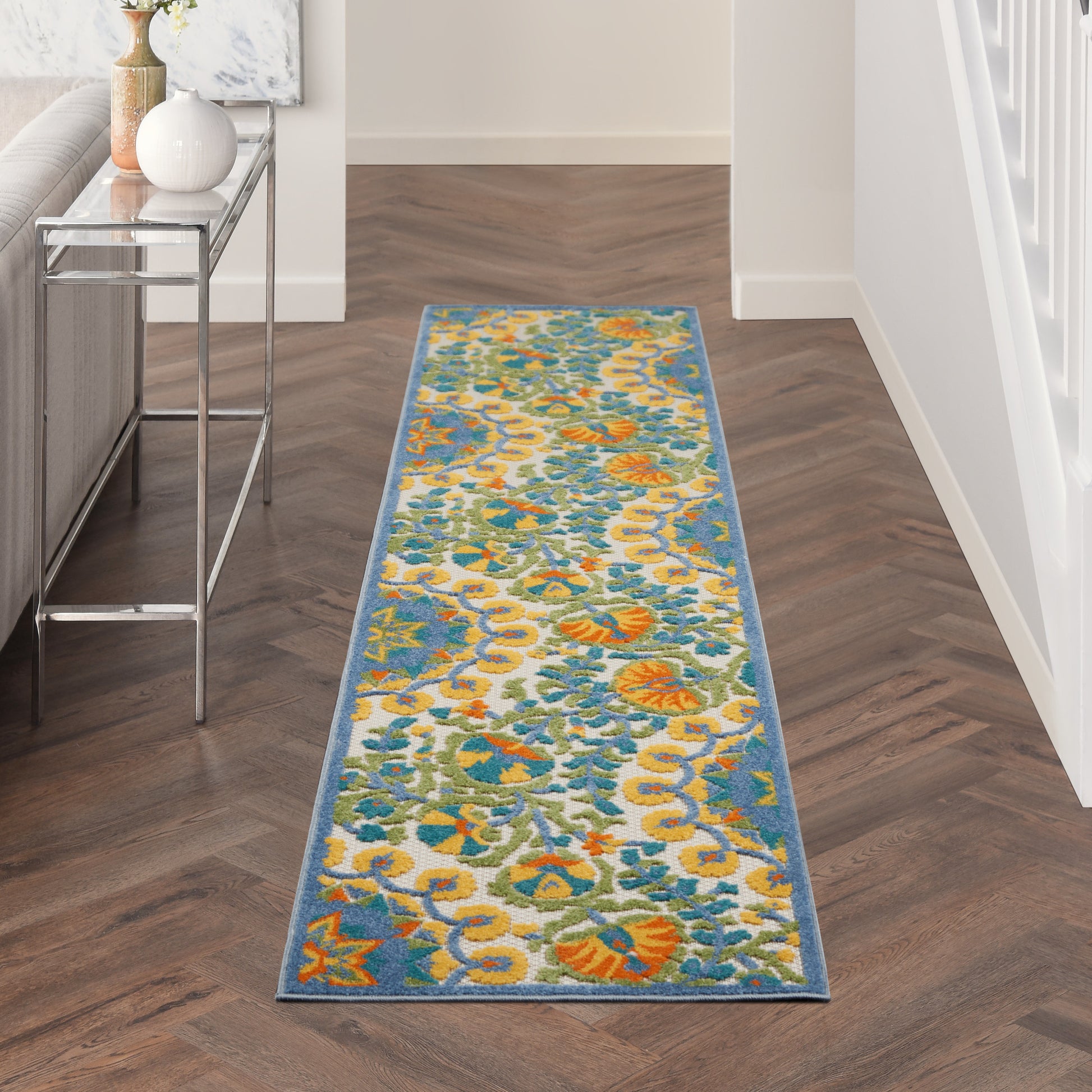 Rectangular floral hallway runner rug in teal, orange, yellow and ivory with a blue border.