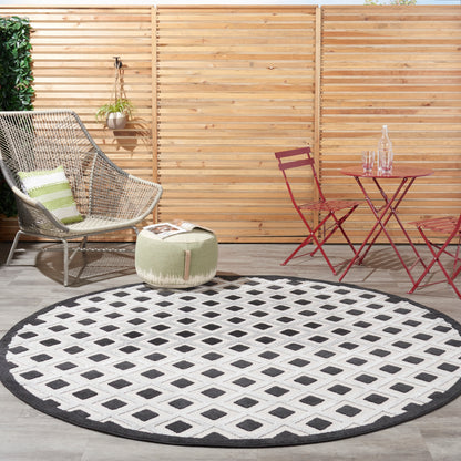 Round black-and-white geometric outdoor rug on a wooden deck with a wicker chair and red metal bistro table.