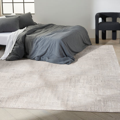Modern bedroom scene showing a light beige rug on the floor, a low bed with a dark gray duvet and pillows, and a black upholstered chair.