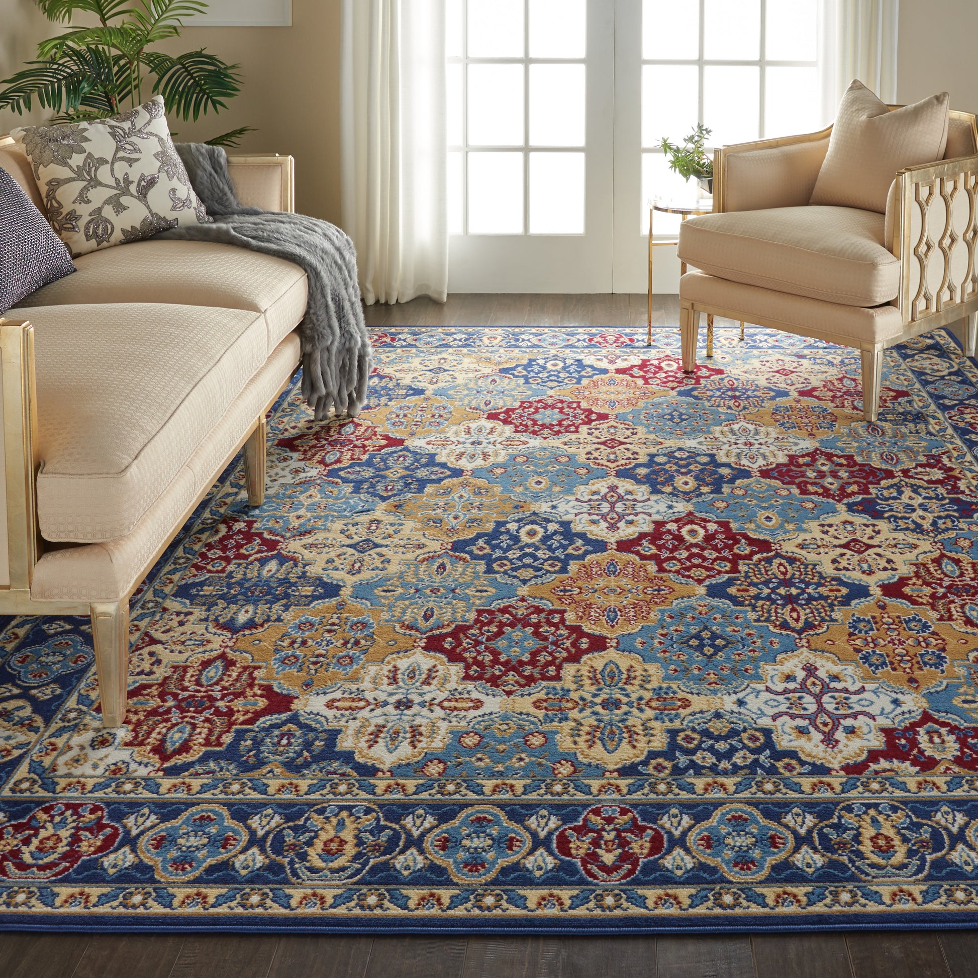 Living room with a vibrant multicolor oriental rug in blue, red, and beige, beige tufted sofas, plant, and French doors.