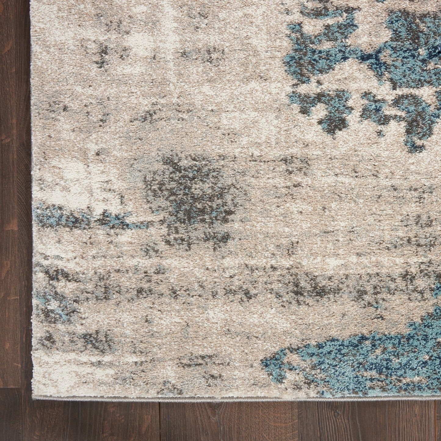 Beige distressed area rug with blue-gray abstract pattern on dark wood floor; left edge visible.