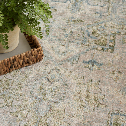 Fern in beige pot on a woven basket atop a pastel blue-pink-green patterned rug.