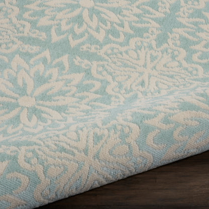 Turquoise and beige damask-patterned rug sample with a folded edge on a dark wood table.