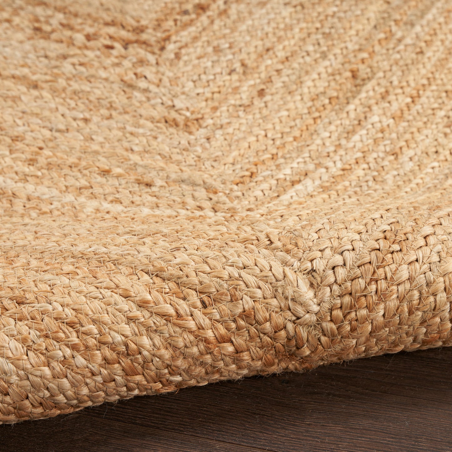 Natural jute rug close-up with woven texture and folded edge on dark wood floor.