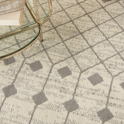 Beige patterned area rug with gray diamond motif under a glass coffee table with brass legs and a stack of books