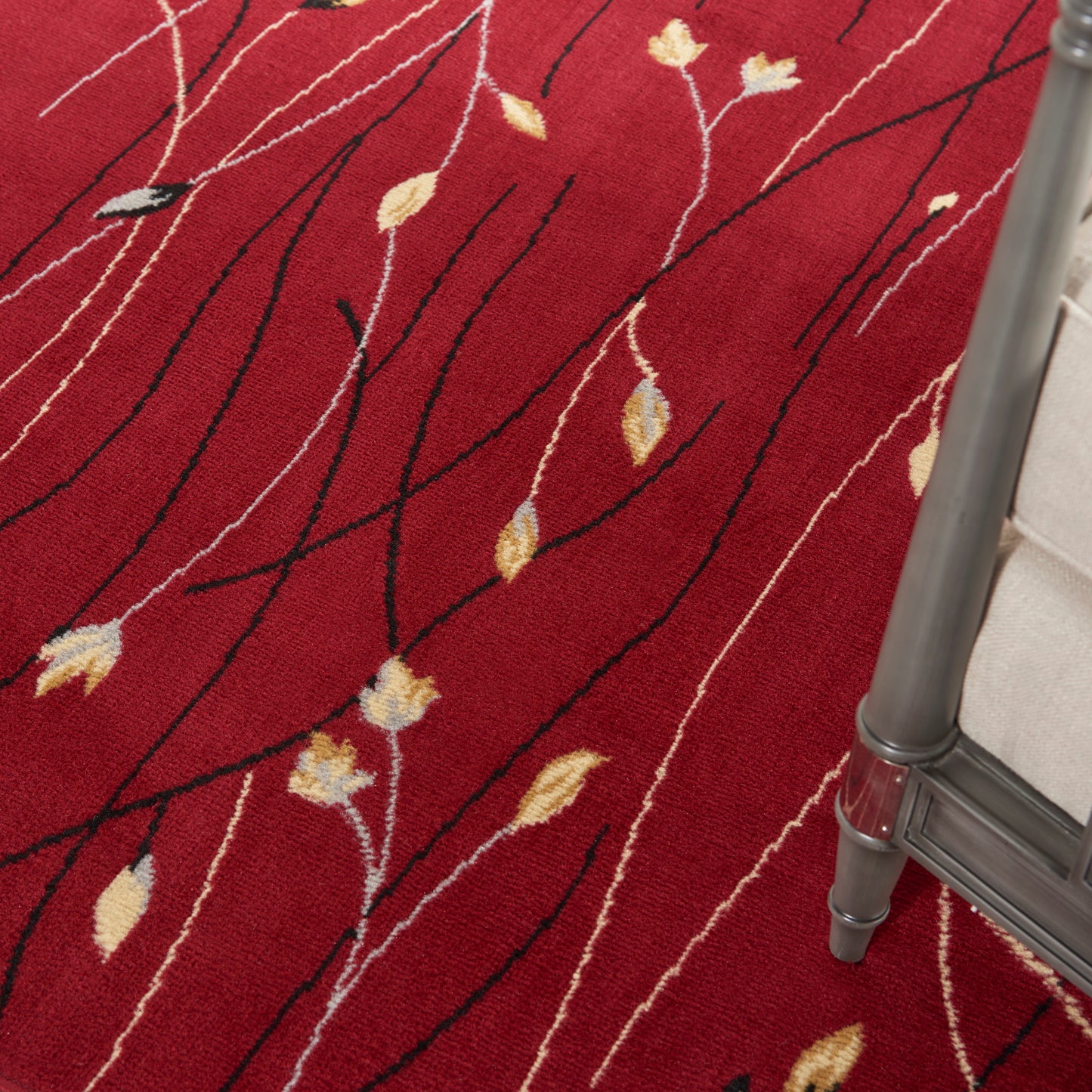 Red patterned rug with black vine-like lines and small yellow leaves; metal-framed chair corner visible.