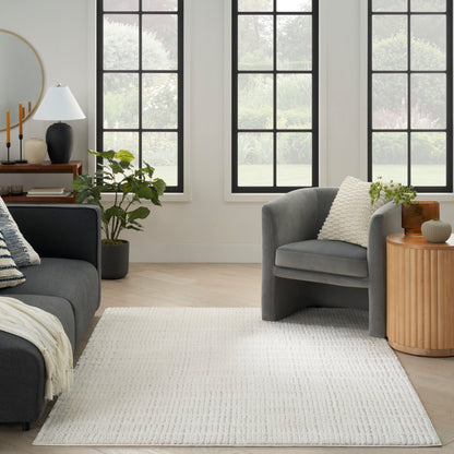 Modern living room with gray sofa and armchair, light wood floor, white rug, black-framed windows, wooden side table.