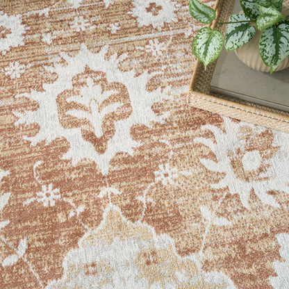 Orange and cream damask-pattern rug; textured weave, corner with a small wicker tray and a potted pothos.