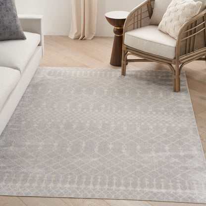 Soft gray geometric patterned area rug in a light living room with a woven rattan chair & light sofa.