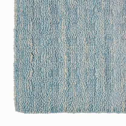 Close-up of a blue and cream shag rug with dense loop pile and variegated light blue fibers.
