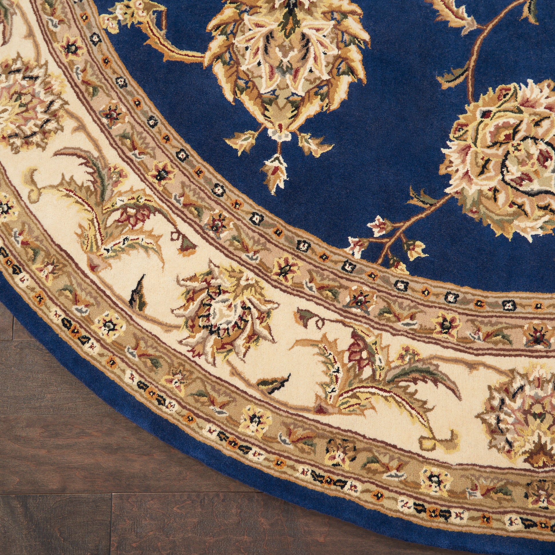 Round oriental rug with deep blue field and ivory-beige floral border on dark wood floor.