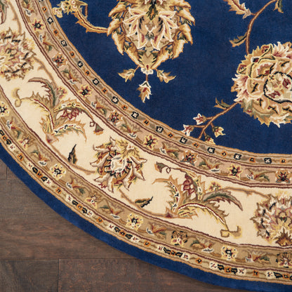 Round oriental rug with deep blue field and ivory-beige floral border on dark wood floor.