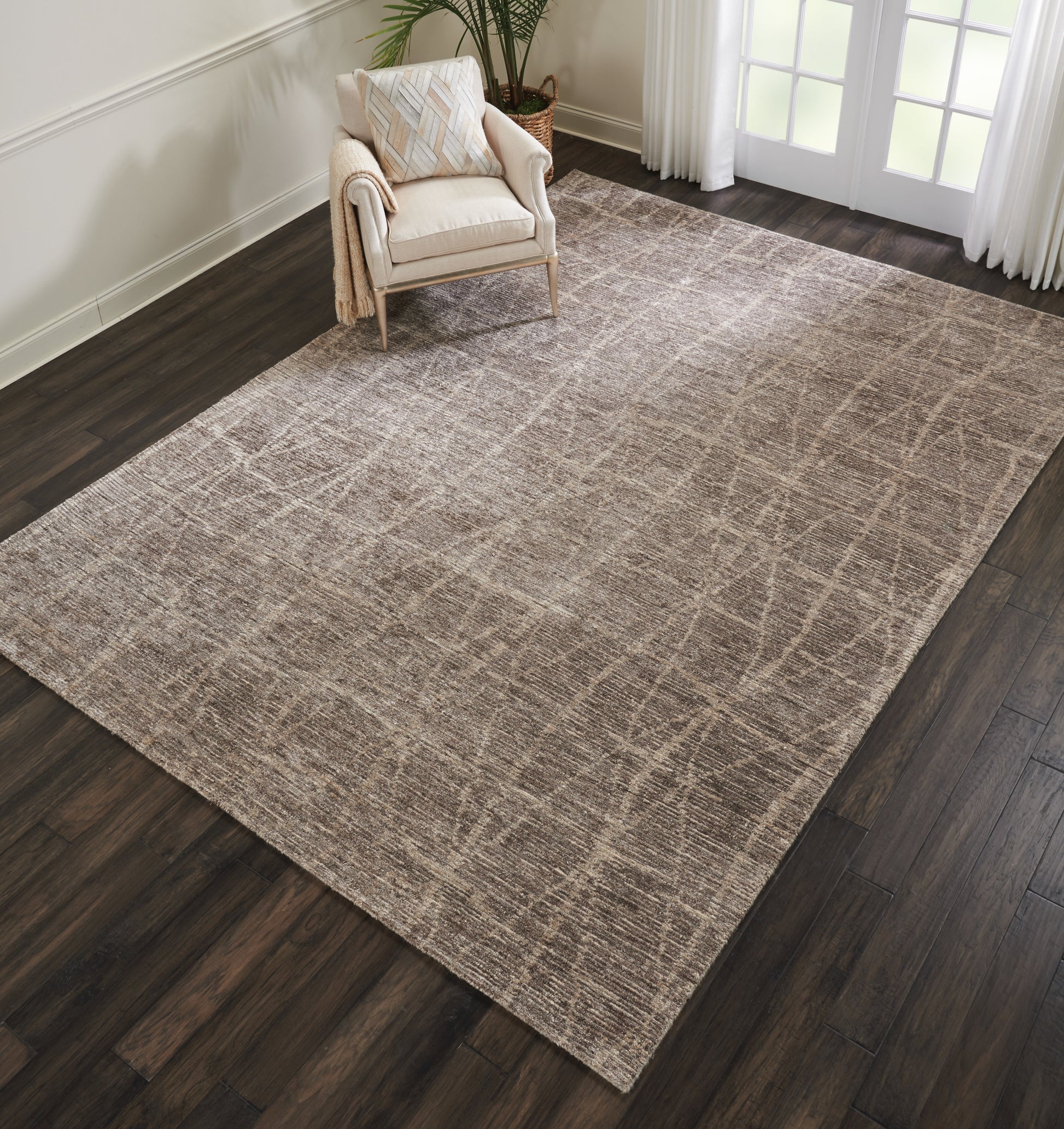 Rectangular taupe area rug with subtle crosshatch grid on dark wood floor, beside beige armchair and glass doors.