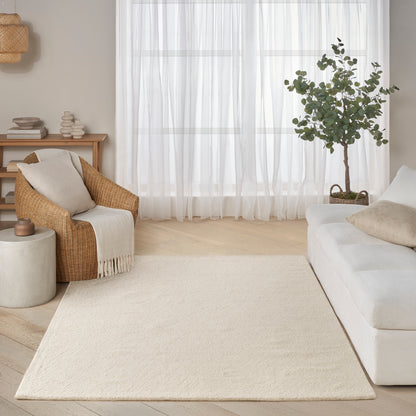 Neutral living room with cream rug, white sofa, wicker armchair, sheer curtains, potted tree, and light wood floors.