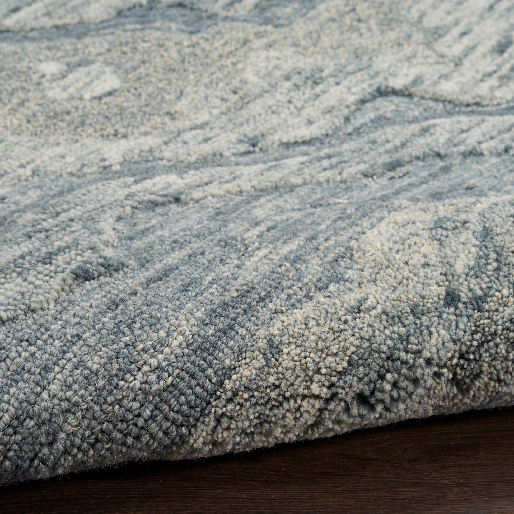 Blue-gray textured rug with boucle loops and soft plush pile, close-up showing thick fiber pattern on dark wood floor.