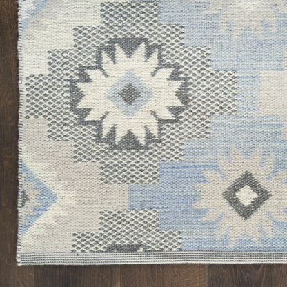 Light blue, ivory and gray geometric kilim rug with starburst and diamond medallions on a wooden floor.