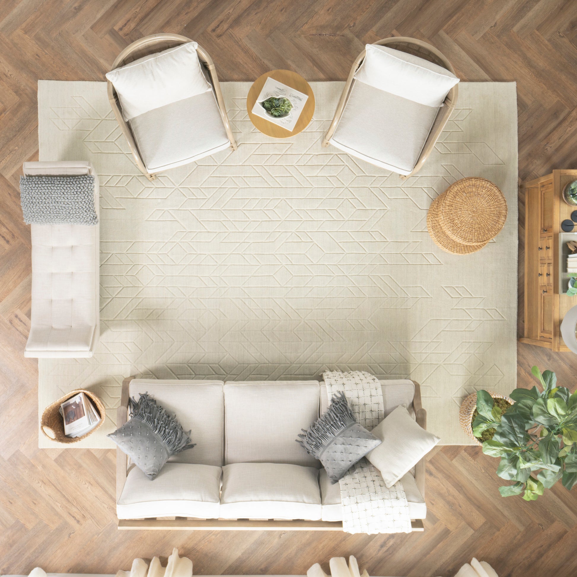 Top-down view of a beige living room with cream sofa, gray cushions, two wicker chairs, geometric rug, round woven mat.