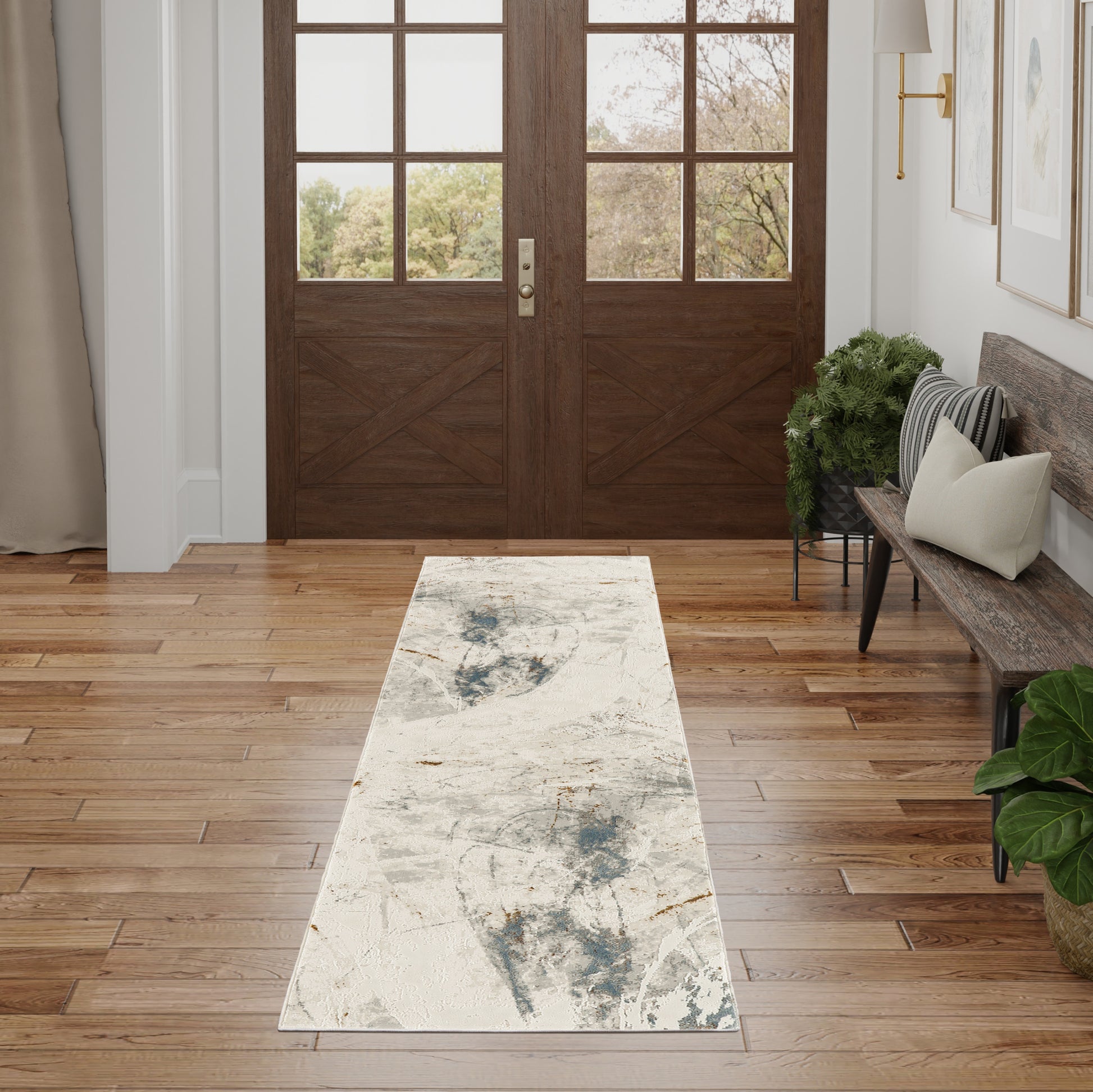 Double wooden entry doors with glass panels, abstract blue-gray runner rug, hardwood floor, bench with cushions, plants.