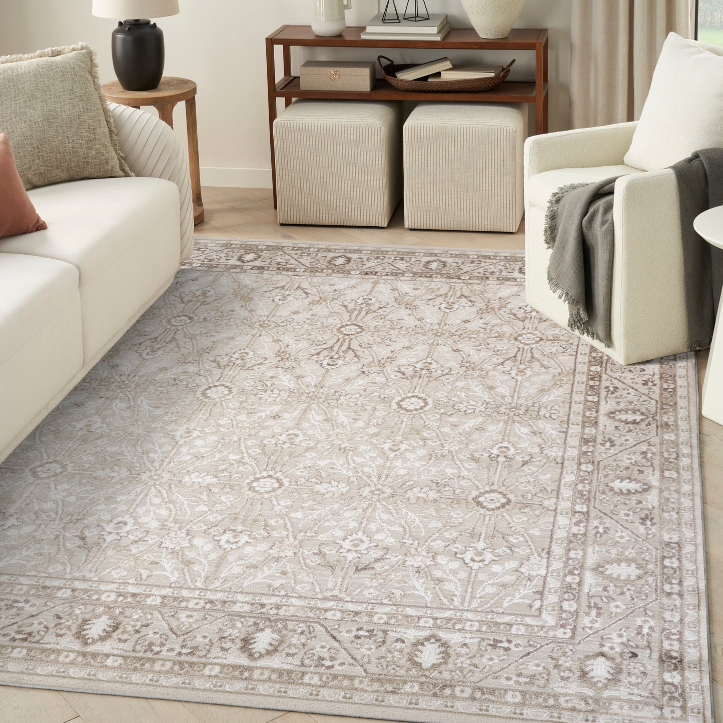 Soft beige patterned area rug with intricate border in a neutral living room featuring cream sofa and light armchair.
