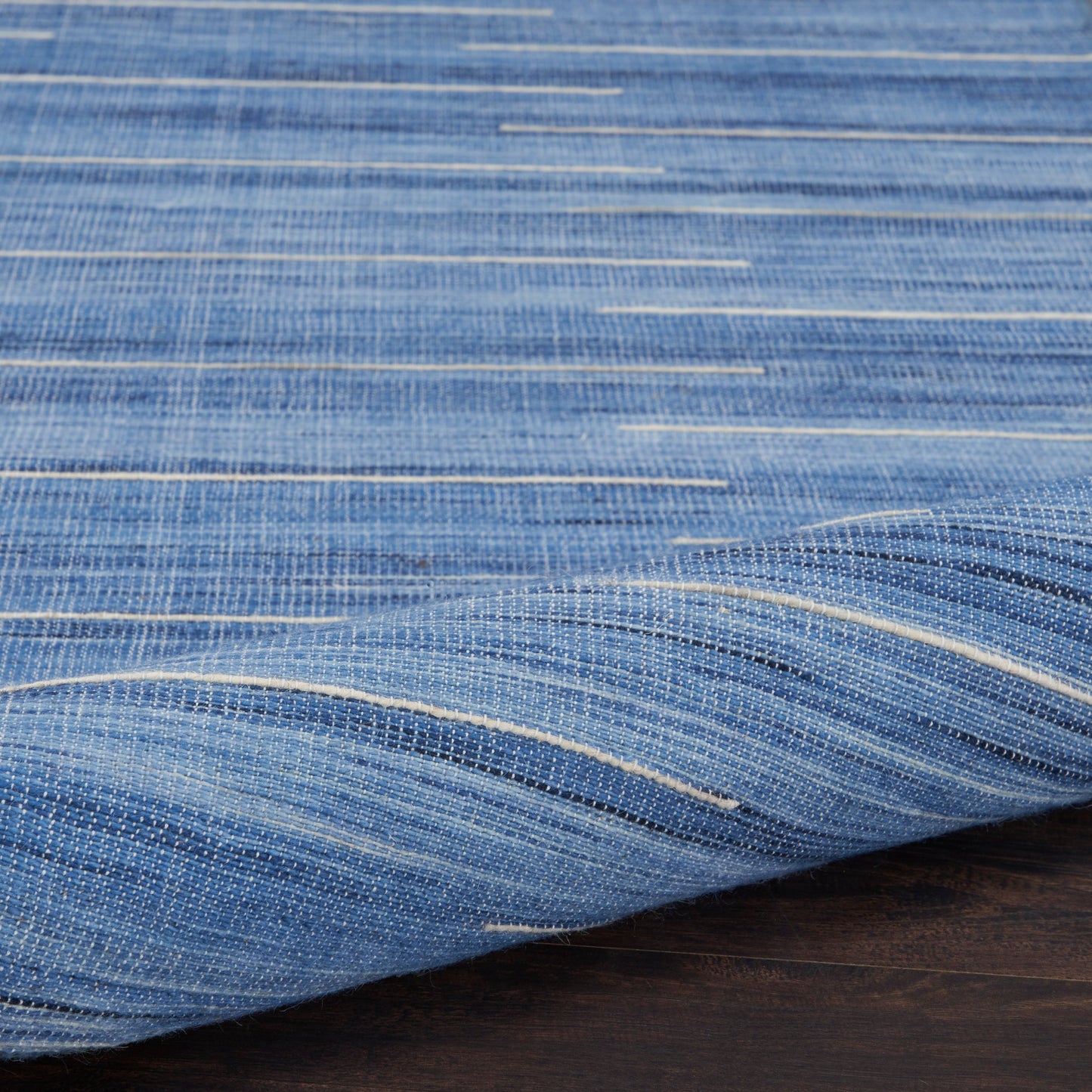 Blue woven denim-style rug with light cream stripes, folded on a dark wood surface.