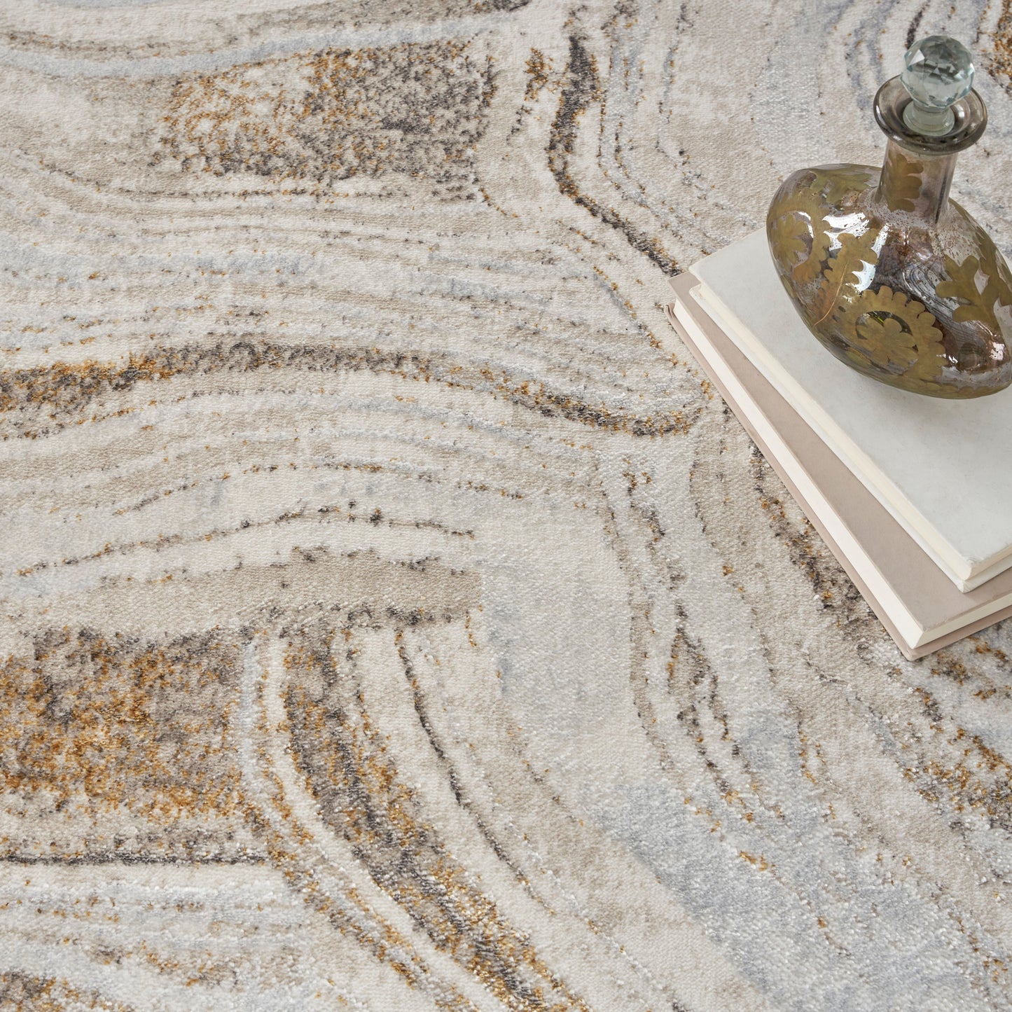 Beige and gray abstract patterned rug with a vintage glass decanter atop stacked light-colored books.