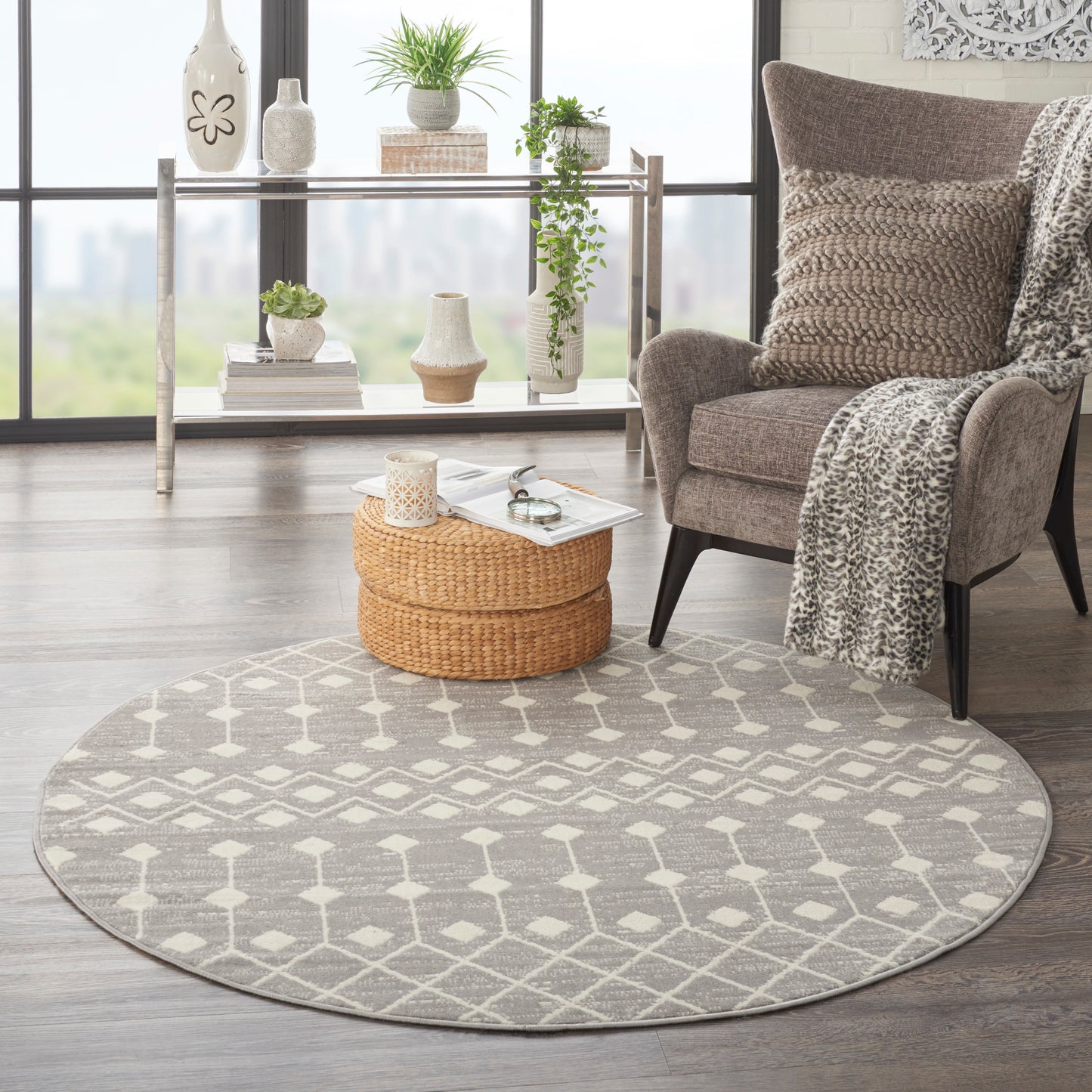 Round gray geometric rug in a bright living room with beige armchair, leopard throw, and a wicker ottoman.