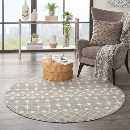 Round gray geometric rug in a bright living room with beige armchair, leopard throw, and a wicker ottoman.