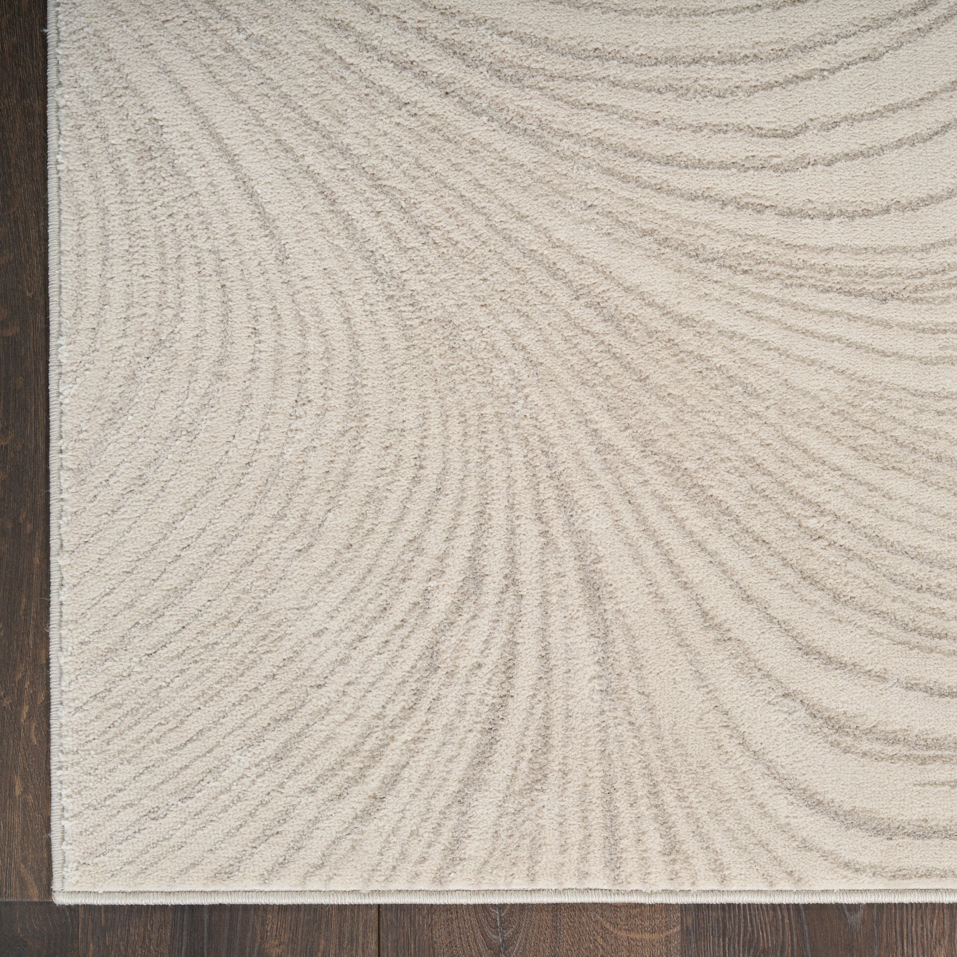 Beige textured rectangular rug with a curved ripple pattern on a dark wooden floor.