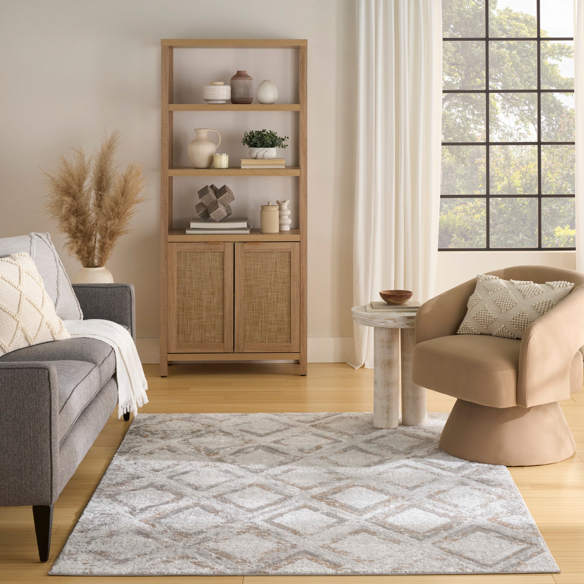 Geometric rug in a living room scene with grey sofa, beige curved armchair, round side table, light wood furniture and a grid window.