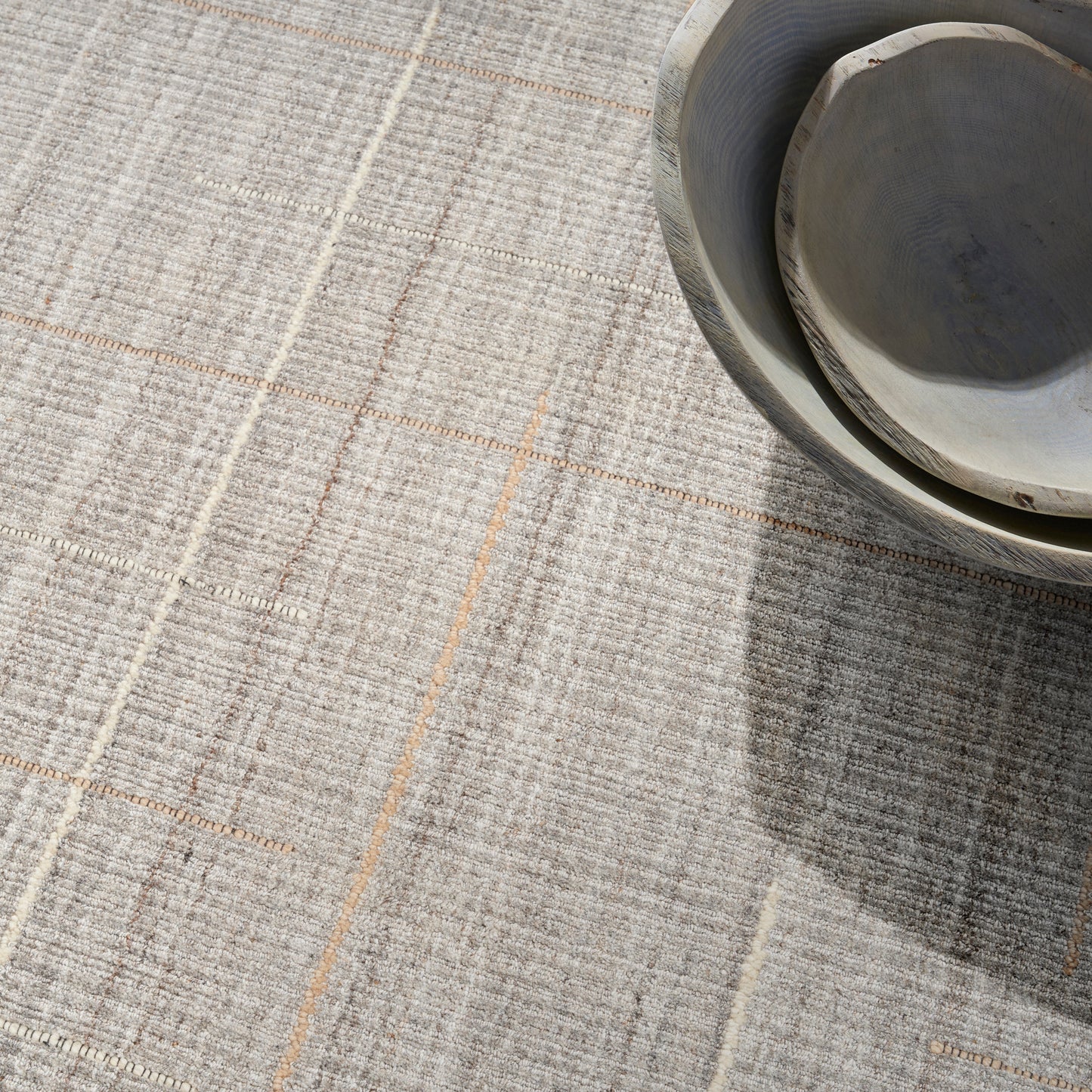 Light gray textured rug with beige plaid lines; partial ceramic bowl in the top-right corner with a soft shadow.