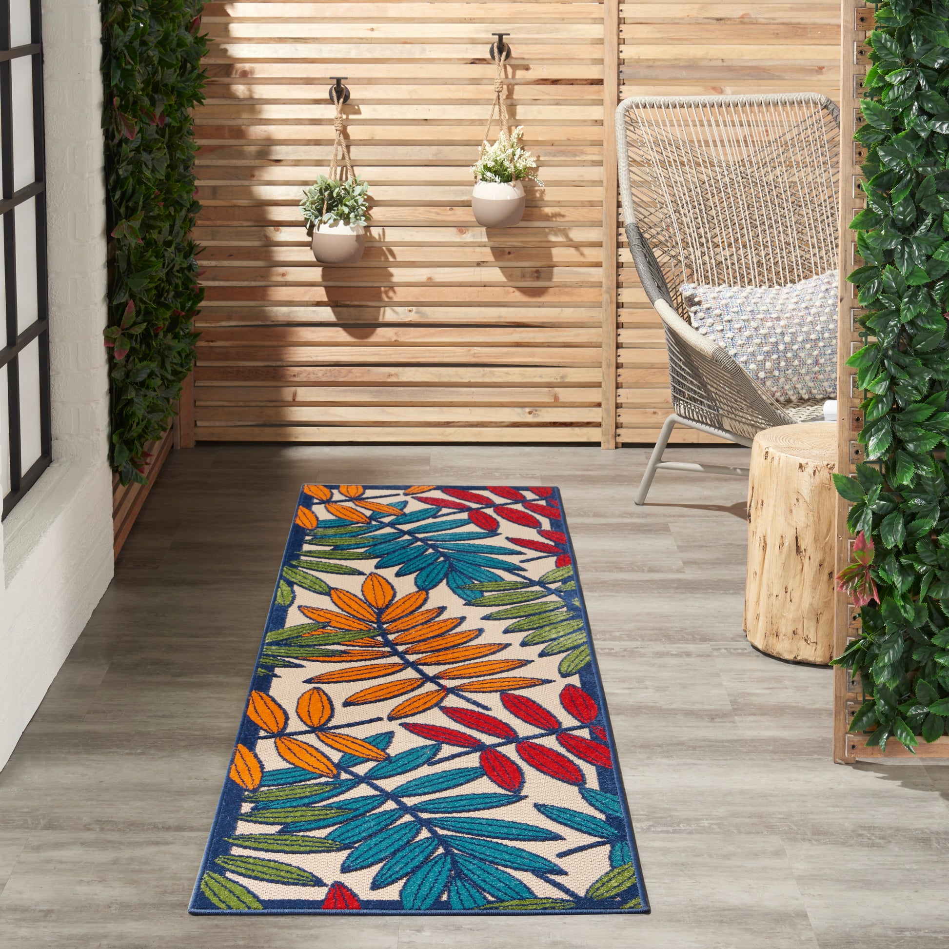 Outdoor rectangular runner rug on a wooden deck with a vibrant tropical leaf pattern in blues, greens, oranges and reds.