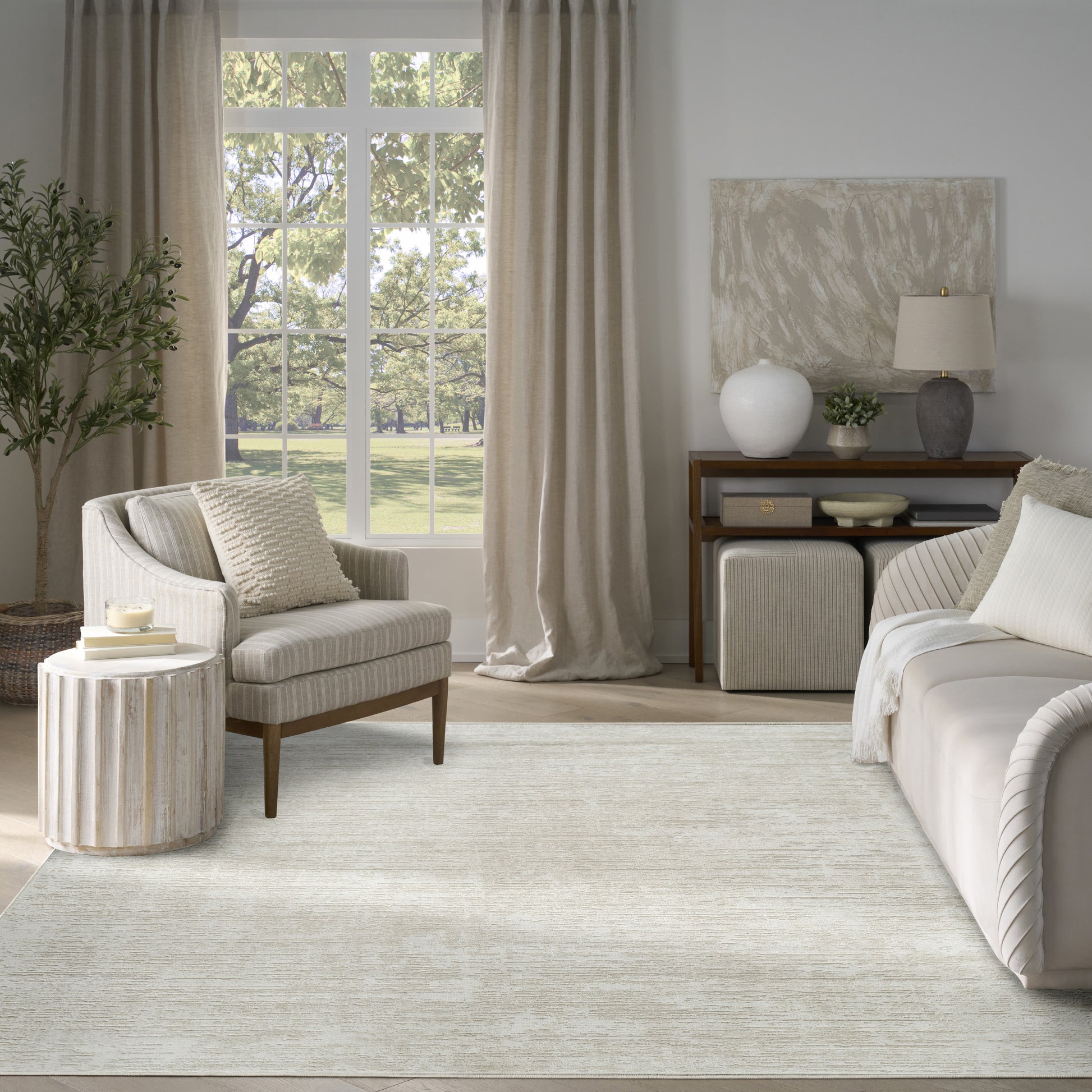 Neutral living room with a light beige area rug, cream sofa, striped armchair, and wooden console under a large window.