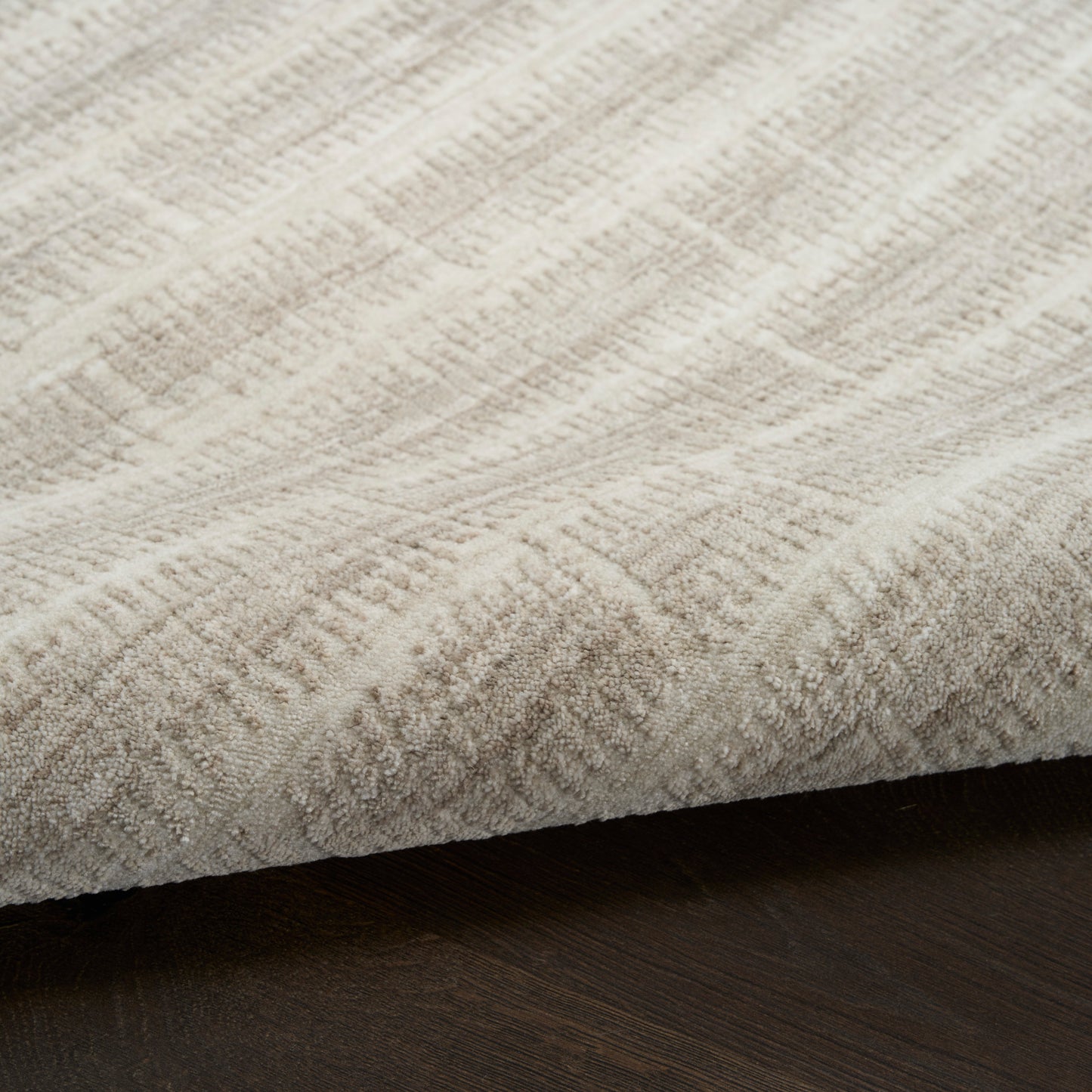 Beige textured area rug with subtle geometric pattern & soft loop pile on dark wood floor.