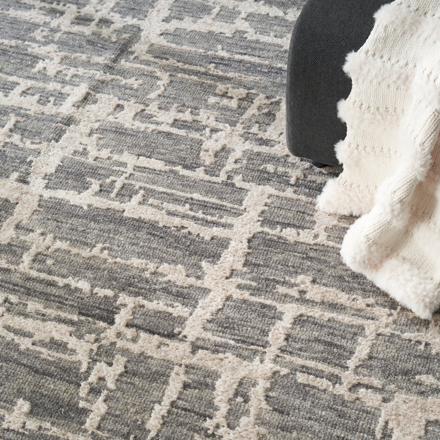 Grey & beige geometric rug with a fluffy cream knit throw partly draped over a dark chair.