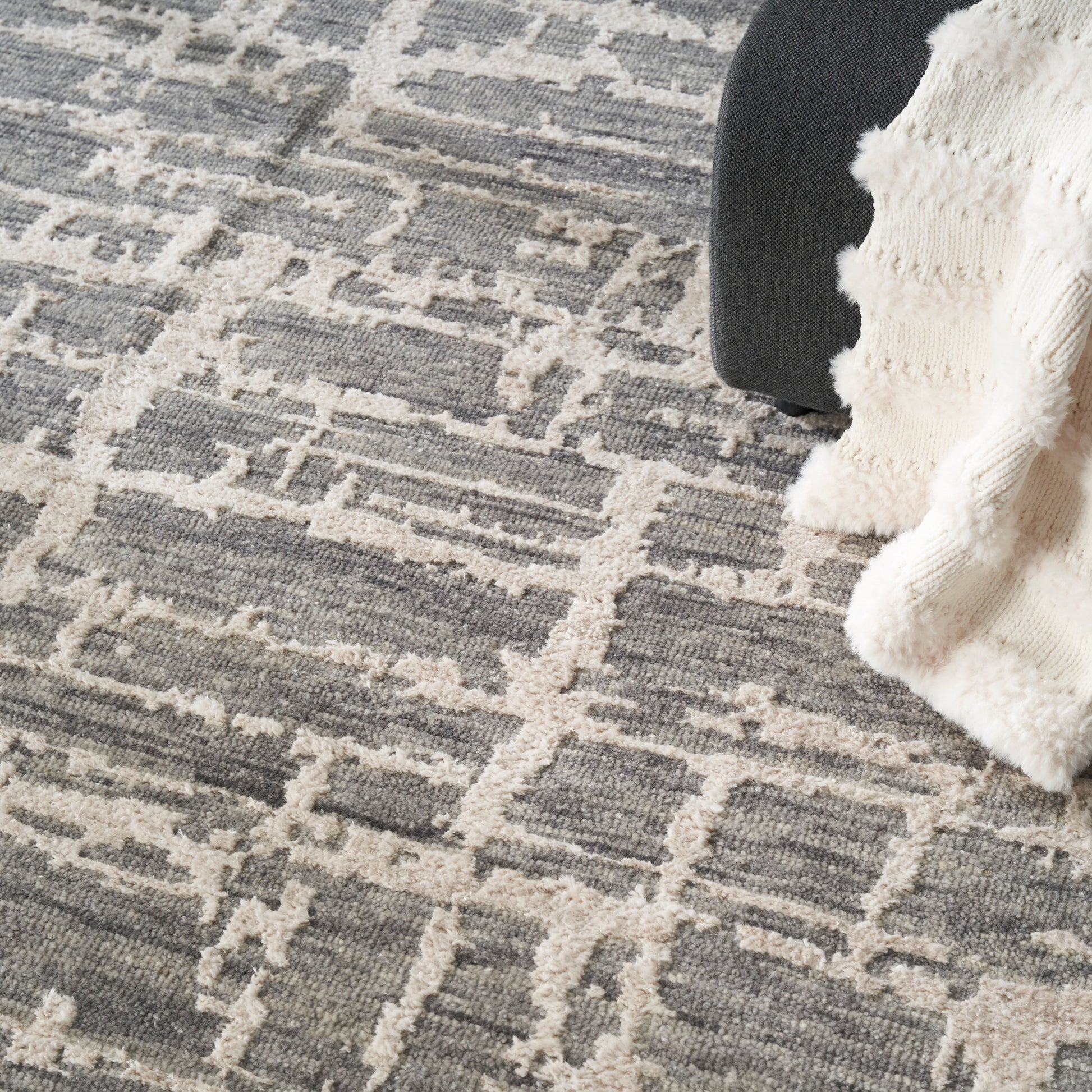 Grey & beige geometric rug with a fluffy cream knit throw partly draped over a dark chair.