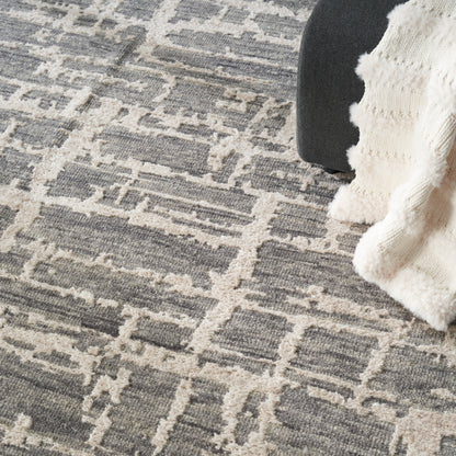 Grey & beige geometric rug with a fluffy cream knit throw partly draped over a dark chair.