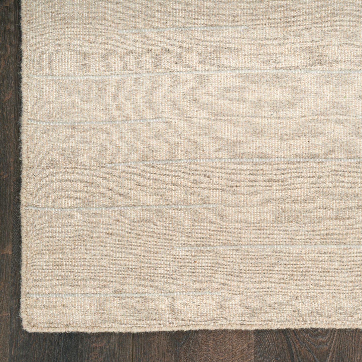 Beige woven rug with subtle horizontal stripes on dark wood floor.